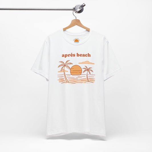 White t-shirt with 'après beach' sunset and palm trees graphic design on a hanger against a white background.