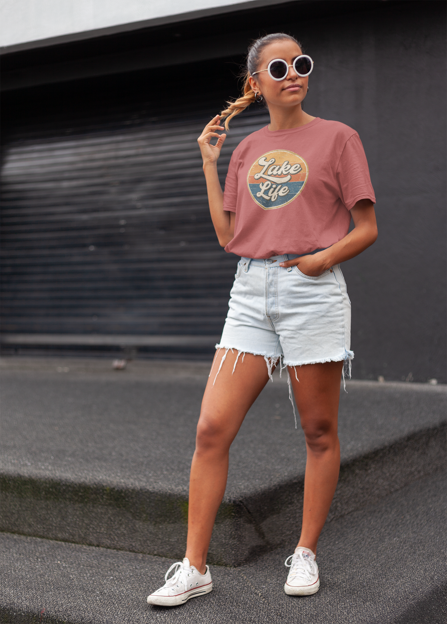 Woman wearing a "Lake Life" graphic t-shirt and denim shorts standing on a rooftop.