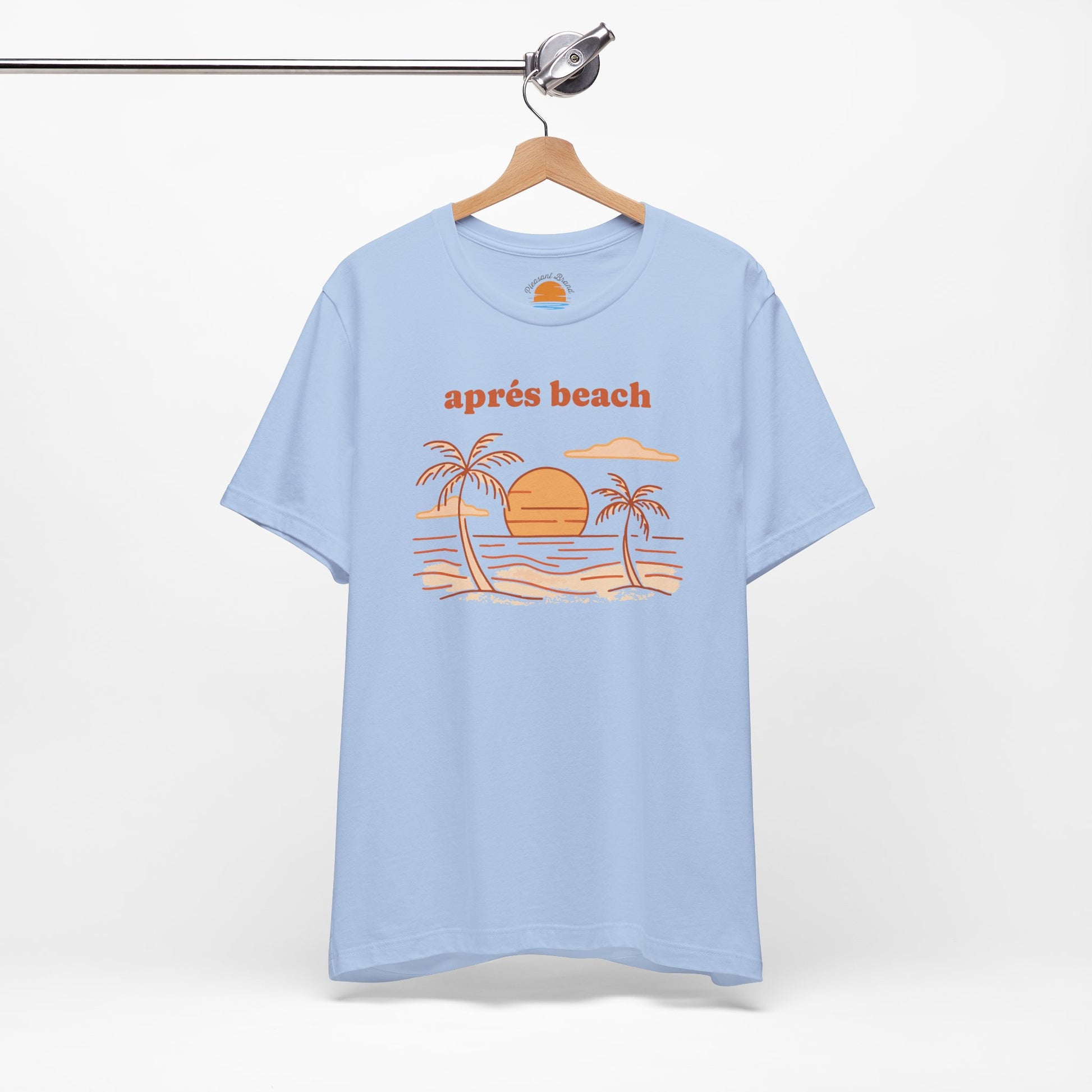 Baby blue color t-shirt with 'après beach' sunset and palm trees graphic design on a hanger against a white background.