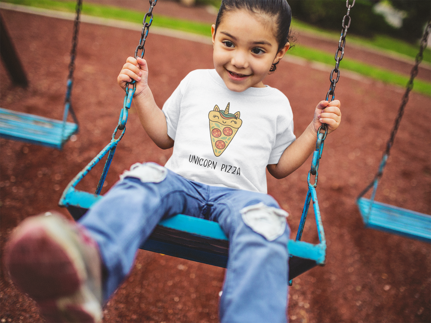 Smiling child in Unicorn Pizza T-Shirt surrounded by colorful art supplies and projects