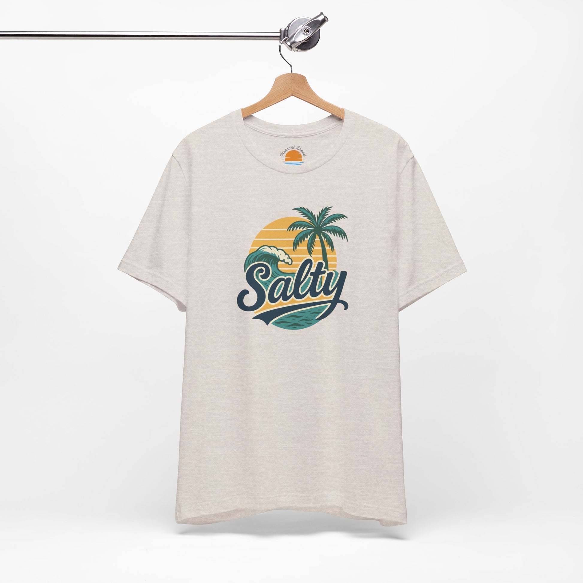 Beige t-shirt with 'Salty' graphic design featuring palm trees and a sunset on a hanger against a white background.
