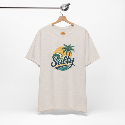 Beige t-shirt with 'Salty' graphic design featuring palm trees and a sunset on a hanger against a white background.