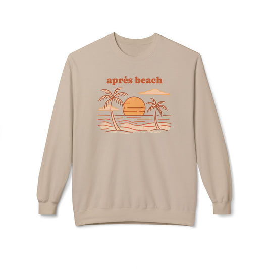 A beige crewneck sweatshirt featuring a retro-style graphic of a beach sunset with palm trees and the text 'après beach' in orange, displayed on a clean white background.