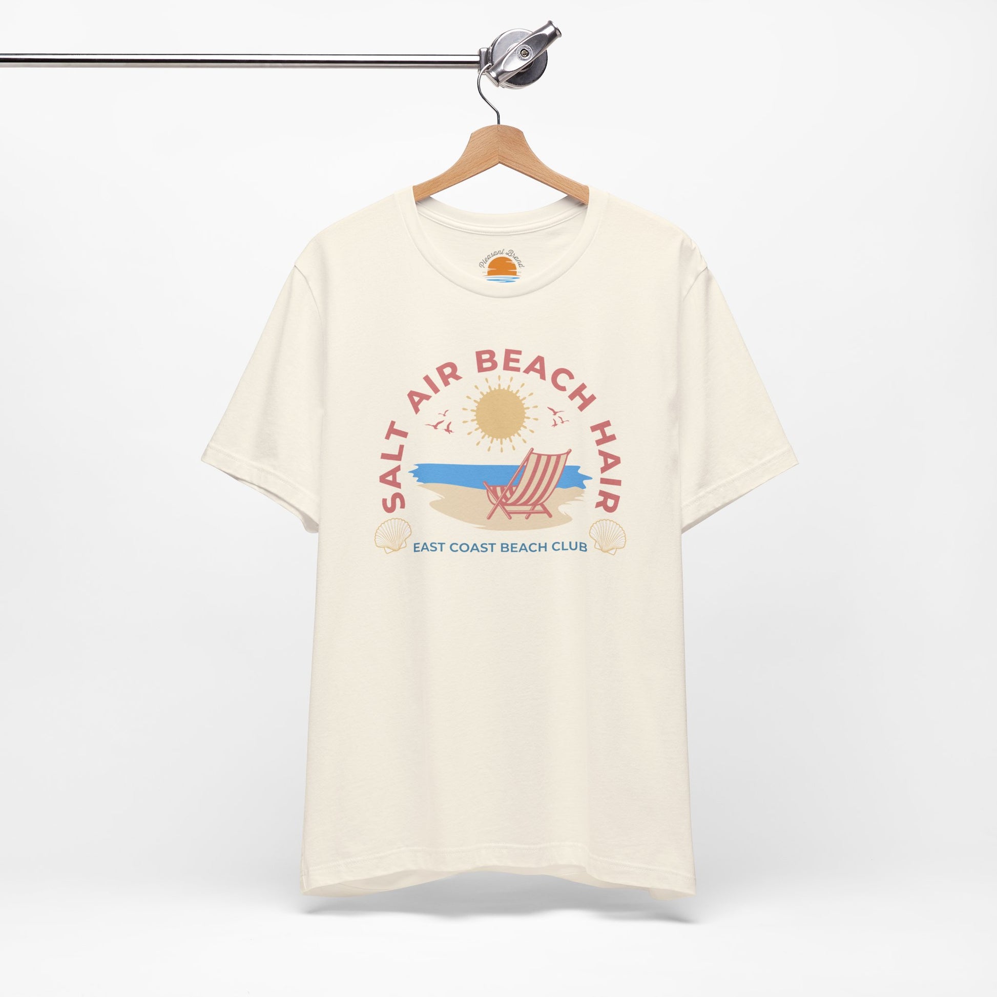 Beige t-shirt with beach-themed graphic on a hanger against a white background