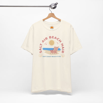 Beige t-shirt with beach-themed graphic on a hanger against a white background