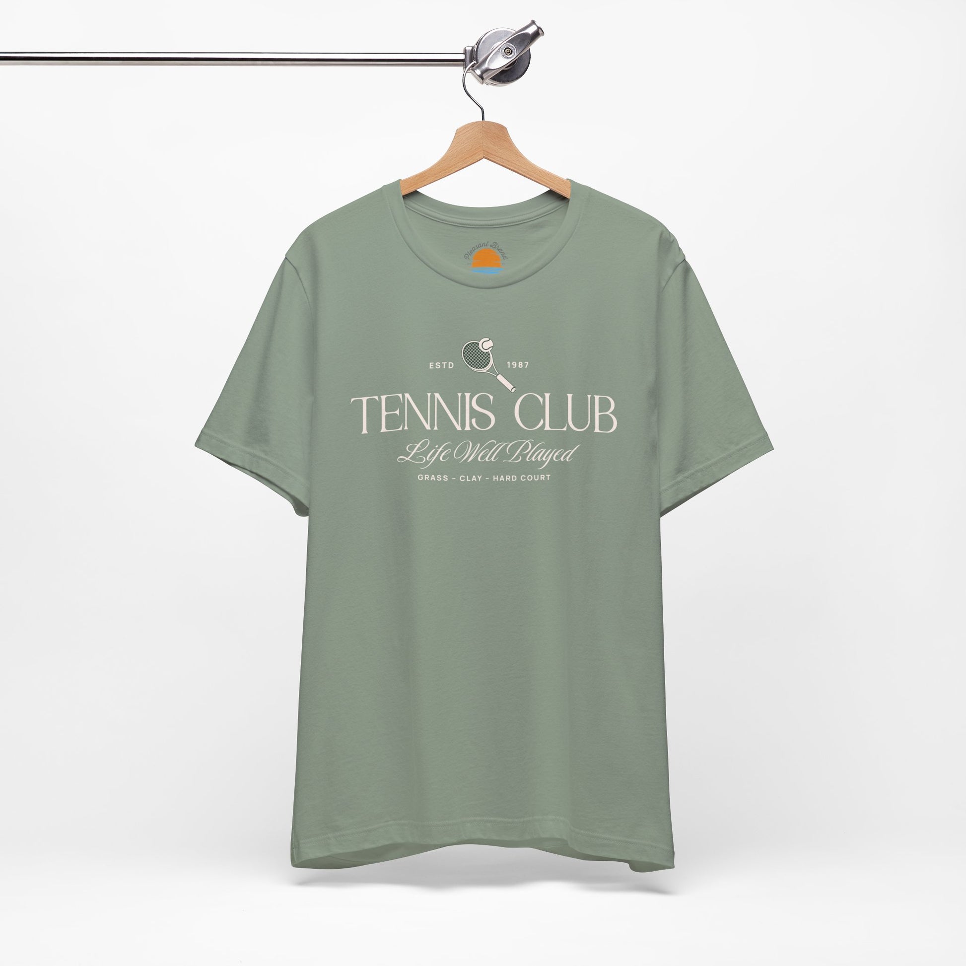 Green t-shirt with 'Tennis Club' text and graphics on a hanger against a white background.