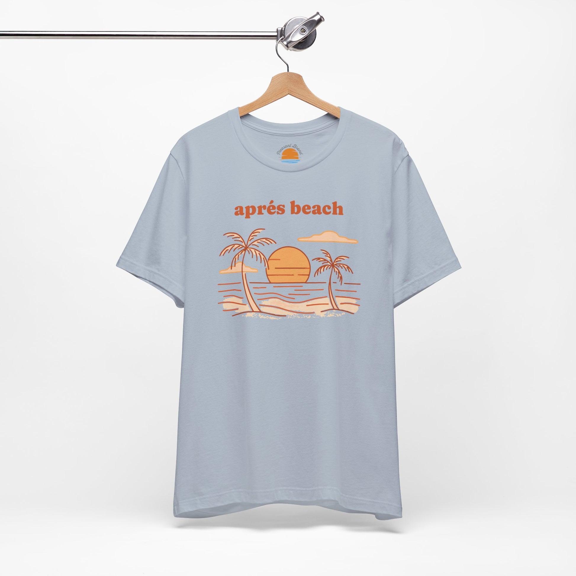 Light blue color t-shirt with 'après beach' sunset and palm trees graphic design on a hanger against a white background.
