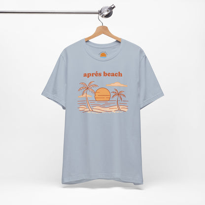 Light blue color t-shirt with 'après beach' sunset and palm trees graphic design on a hanger against a white background.