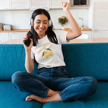 Woman sitting on a blue couch wearing headphones and a white t-shirt with a limoncello design, holding a phone.