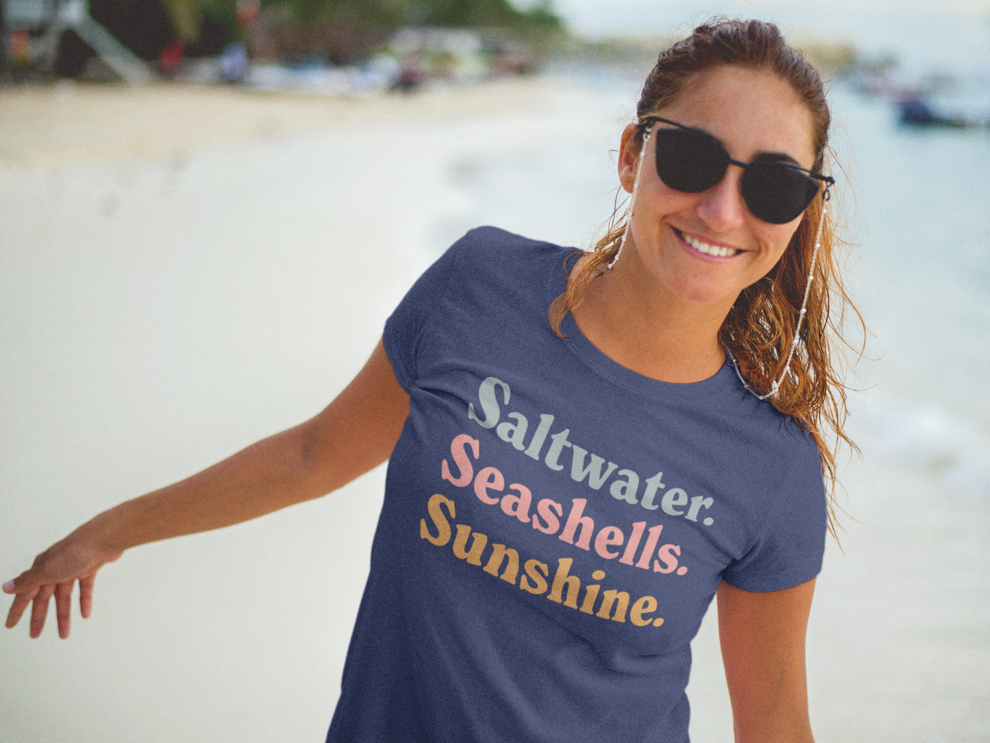 Happy woman wearing china blue Comfort Colors Saltwater Seashells Sunshine T-shirt on beach with sunglasses