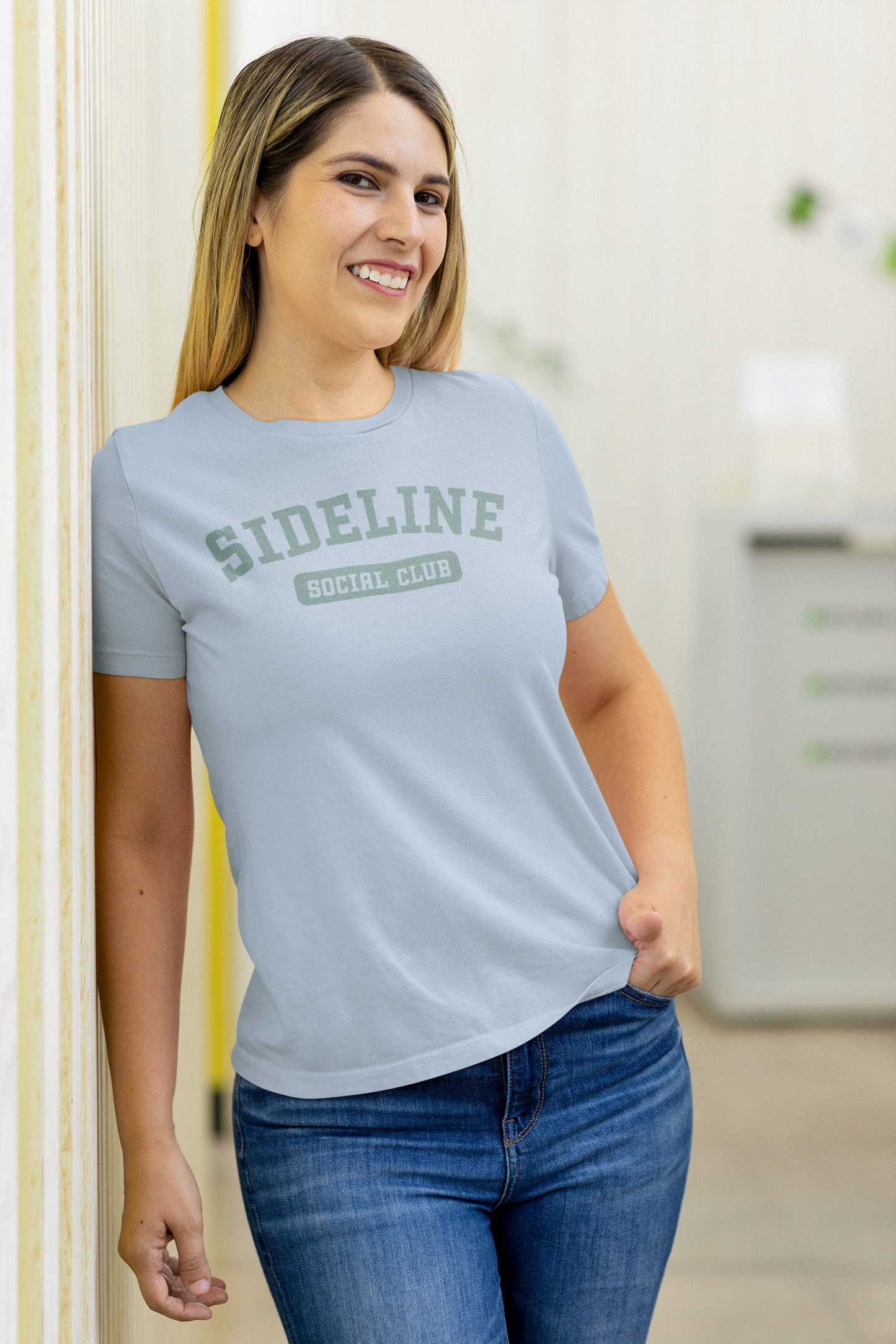 Woman wearing a light blue t-shirt with 'SIDELINE SOCIAL CLUB' text, standing indoors.