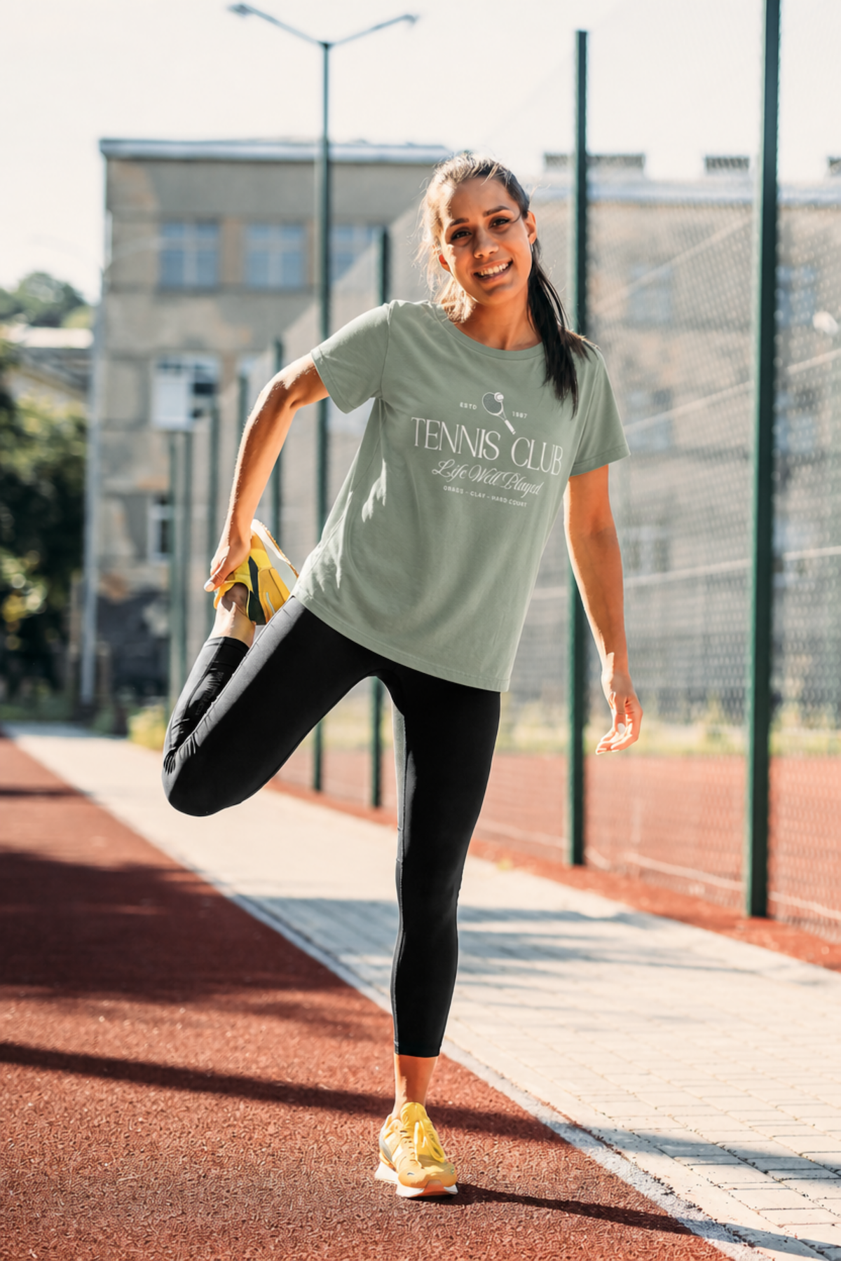 Woman stretching on a tennis court wearing a 'Tennis Club' t-shirt.