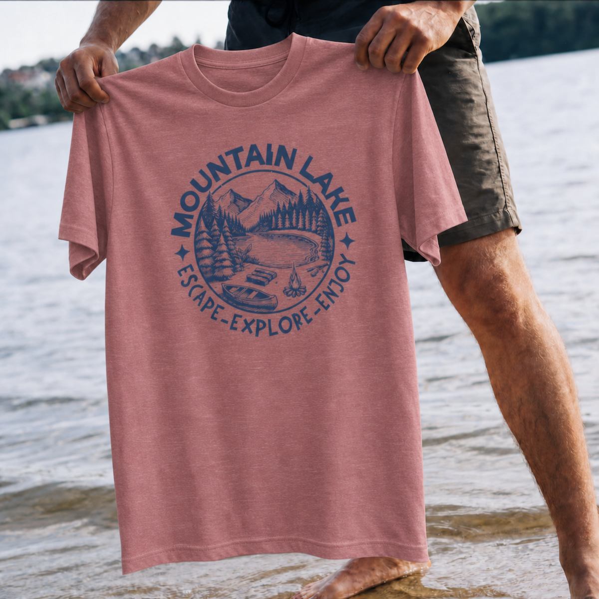 Person holding a pink t-shirt with 'Mountain Lake' design by a lake.