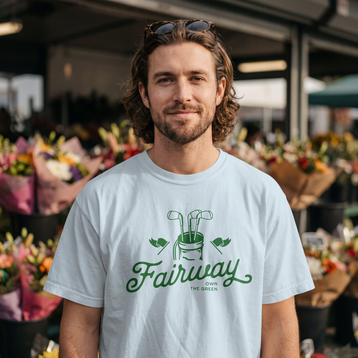 Man wearing a light blue t-shirt with 'Fairway' logo at an outdoor market.