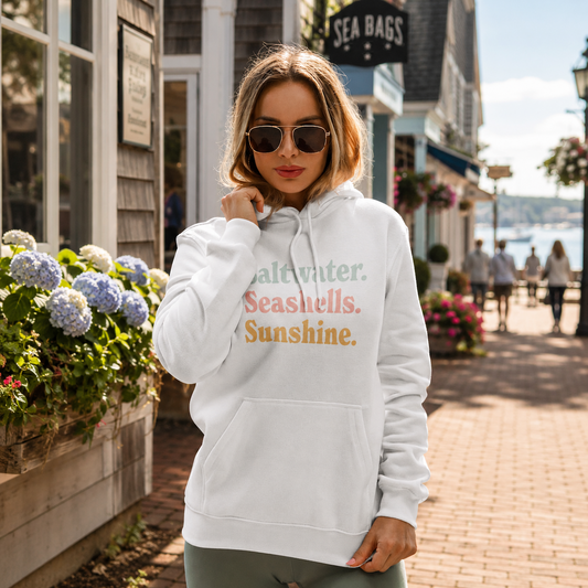 A woman wearing a white pullover hoodie with the text 'Saltwater. Seashells. Sunshine'