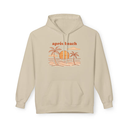 A light beige pullover hoodie, featuring a retro-style orange graphic of palm trees, a sun, and waves with the text 'après beach' printed above it.