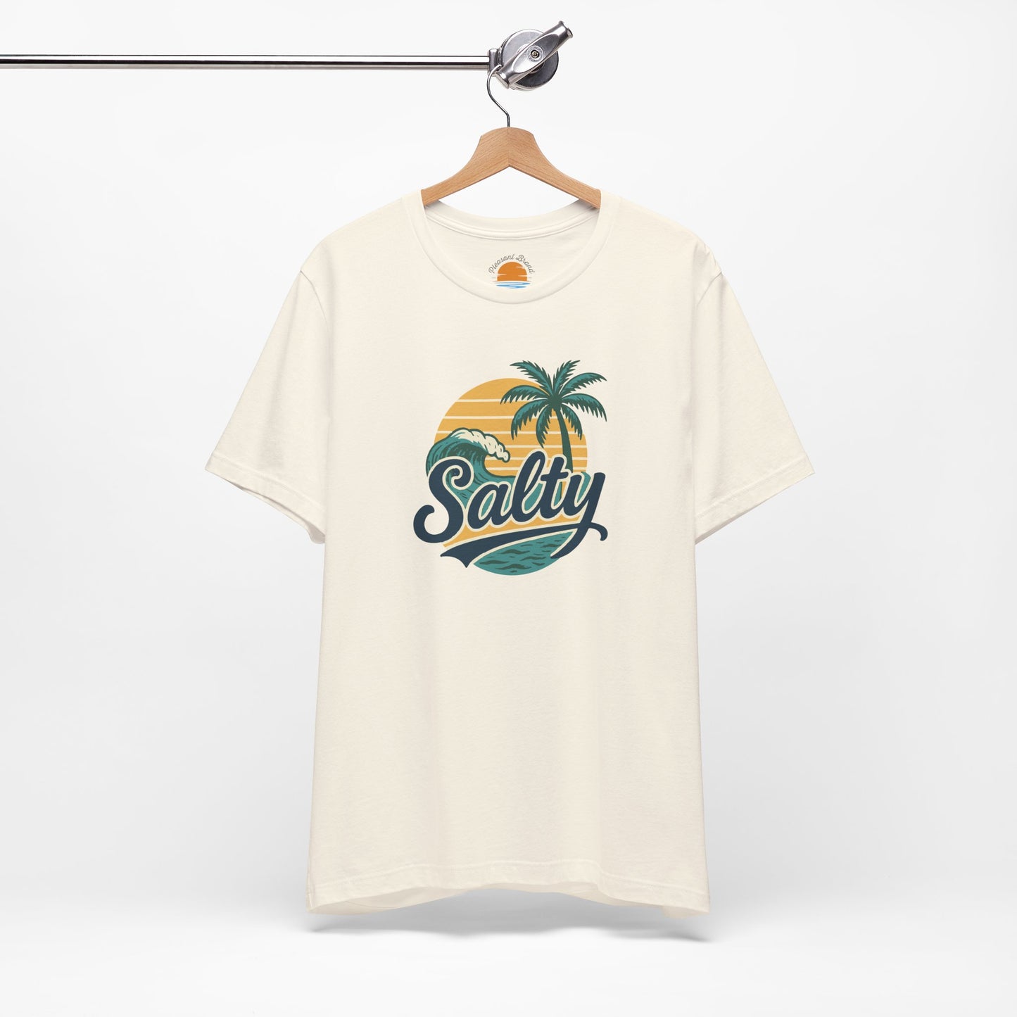 Beige t-shirt with 'Salty' graphic design featuring palm trees and a sunset on a hanger against a white background.