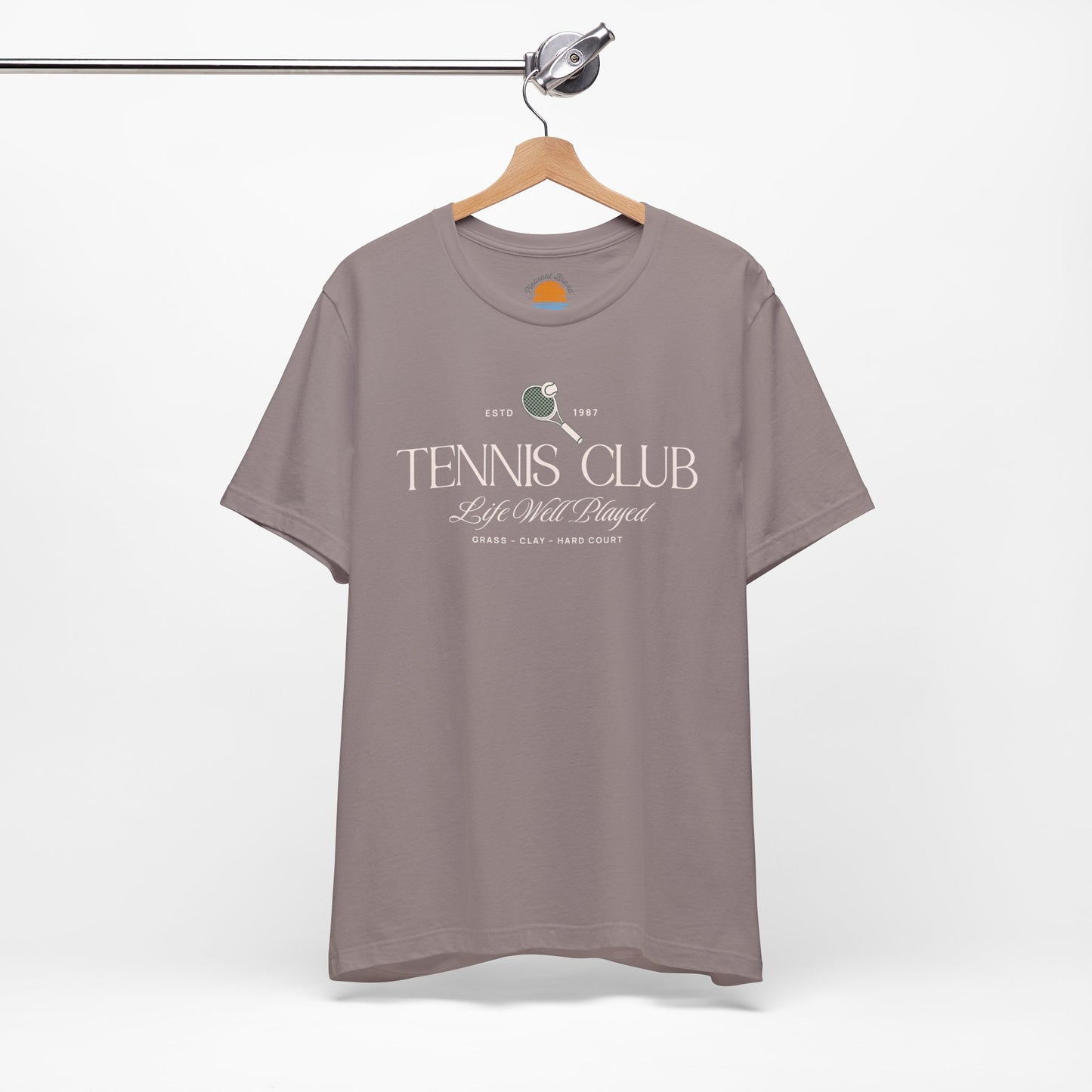 Pebble brown t-shirt with 'Tennis Club' text and graphics on a hanger against a white background