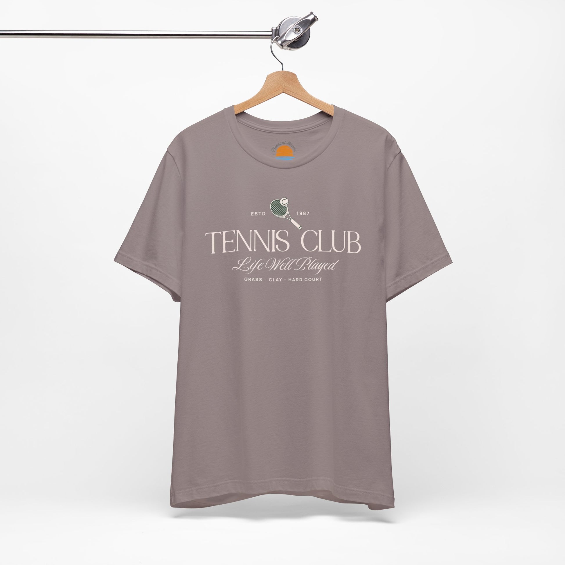 Pebble brown t-shirt with 'Tennis Club' text and graphics on a hanger against a white background