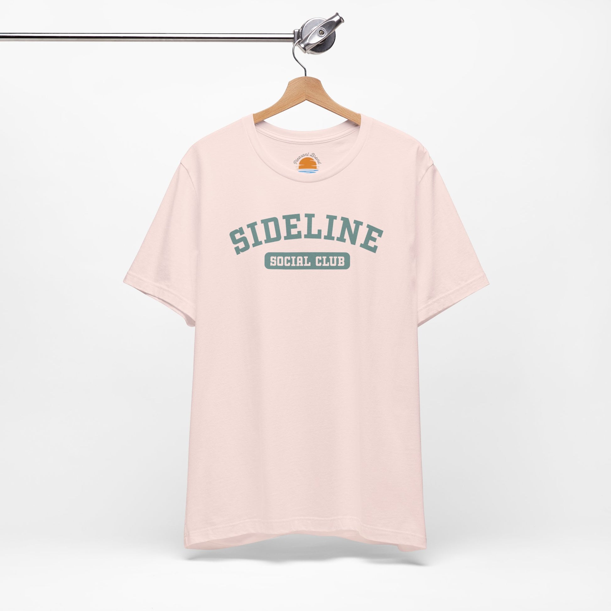 Pink t-shirt with 'Sideline Social Club' text on a hanger against a white background