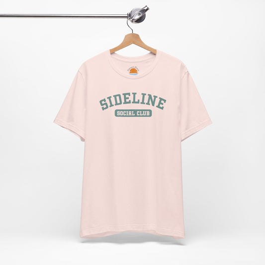 Pink t-shirt with 'Sideline Social Club' text on a hanger against a white background