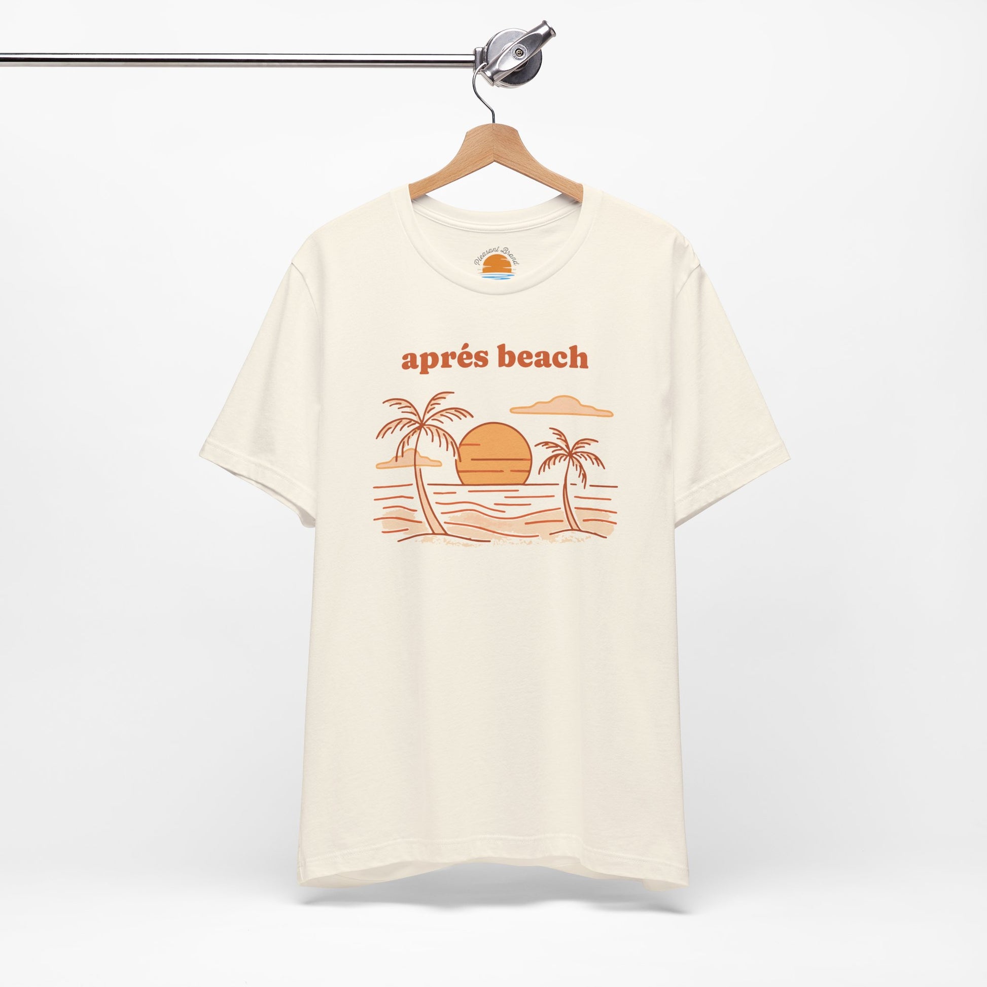 Natural color t-shirt with 'après beach' sunset and palm trees graphic design on a hanger against a white background.